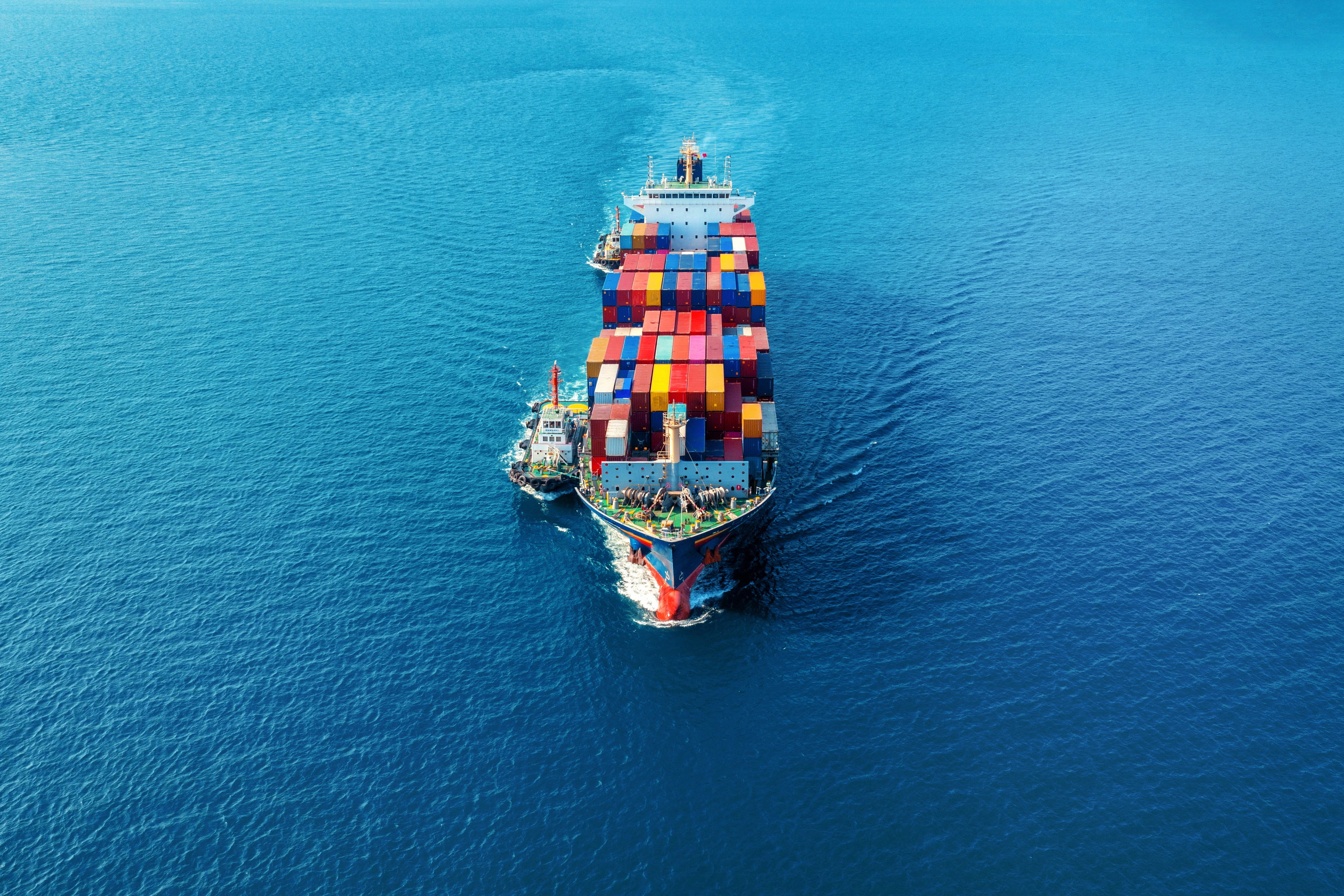 Container ship carrying colorful shipping containers sailing on open sea, aerial view.