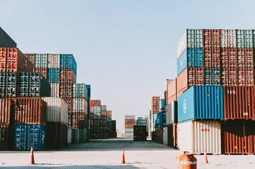 Containrar i rött, blått och vitt som är staplade på varandra längs långa rader.