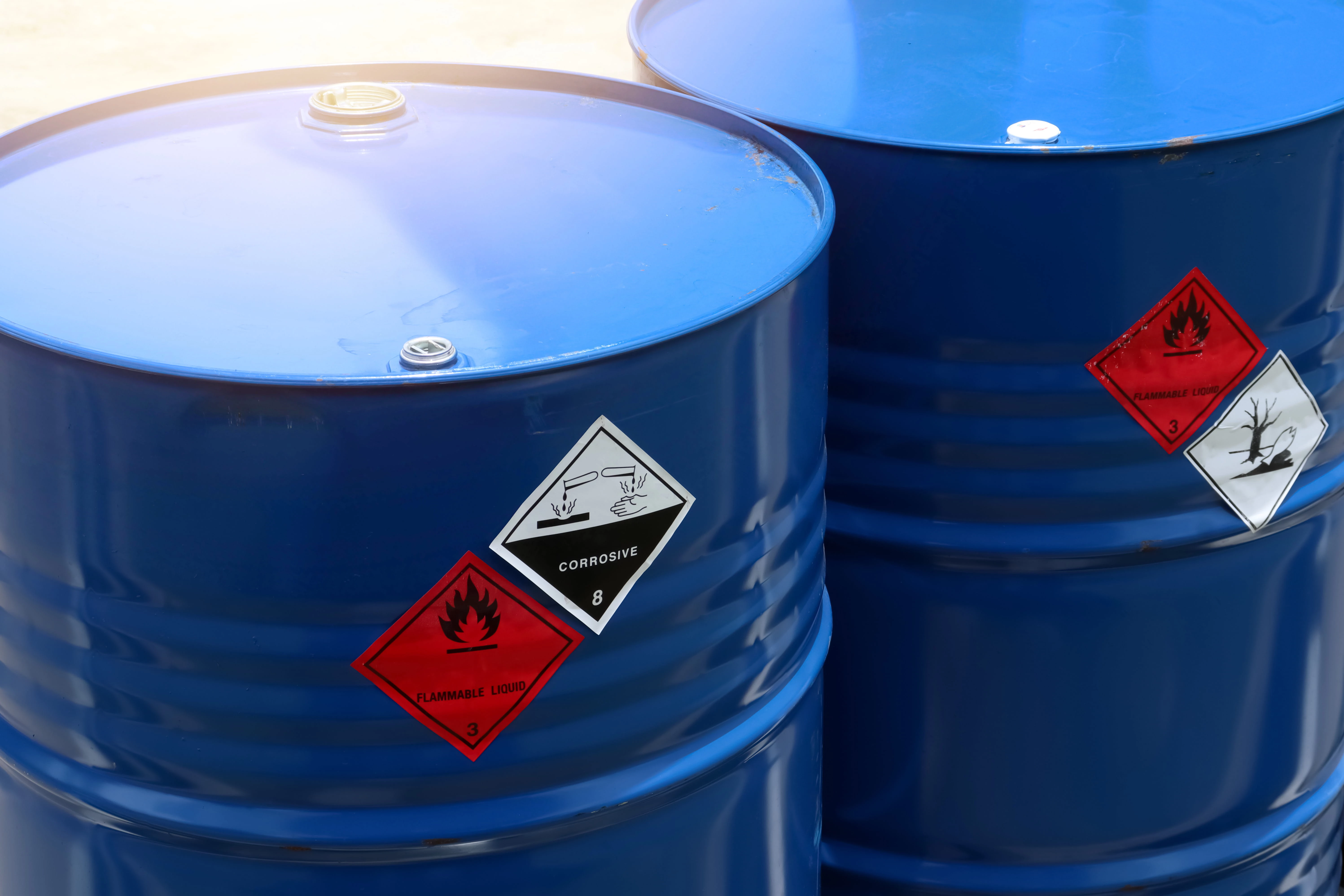 Two blue industrial barrels labeled with hazard symbols for flammable liquid and corrosive substances.