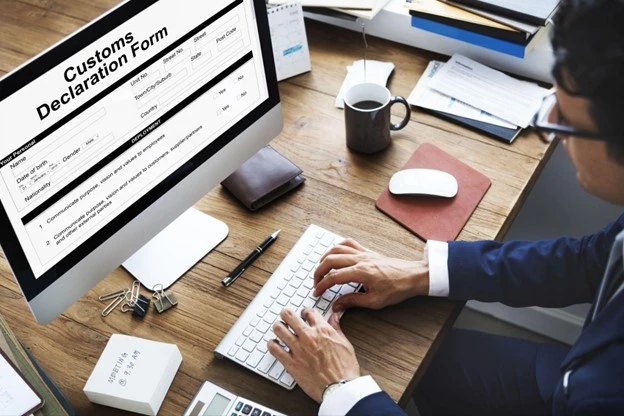 A male person with glasses writing on his computer. On screen shows a customs declaration form
